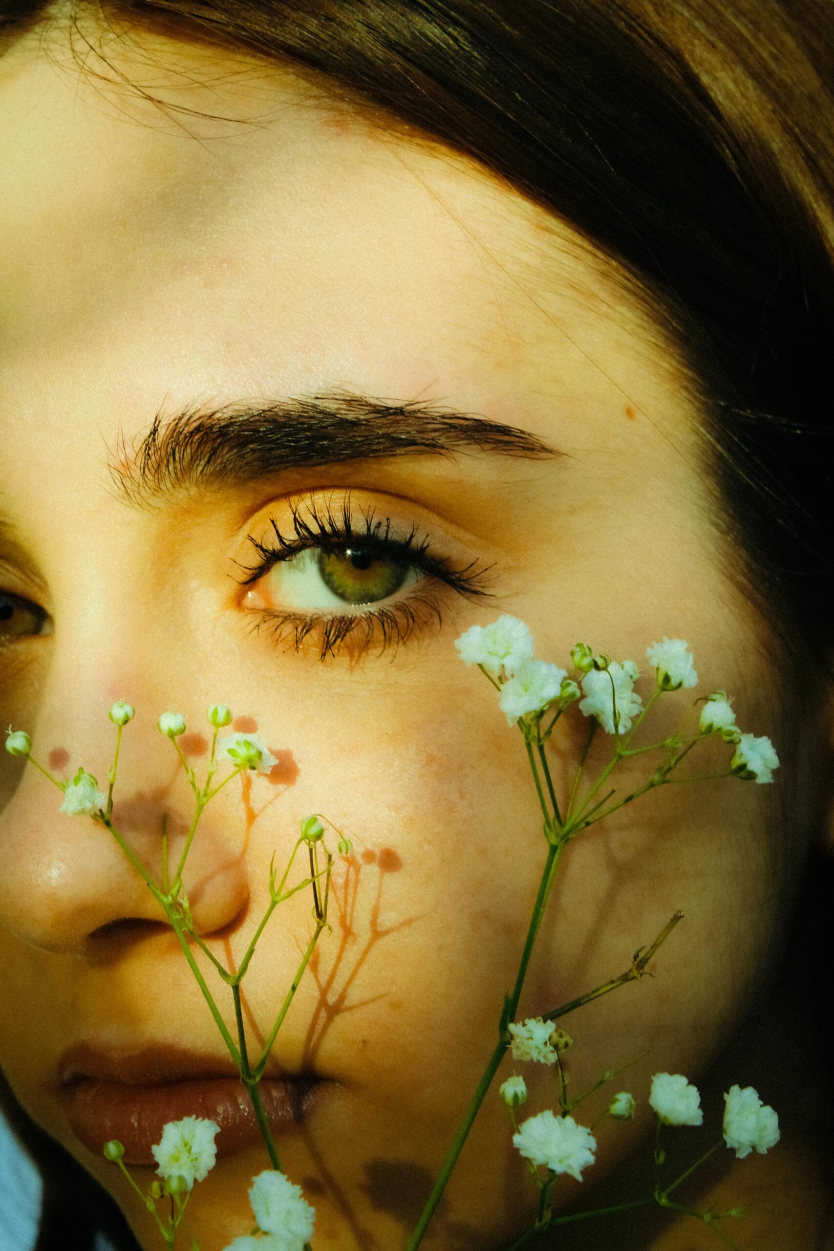 Close-up portrait of a young woman with green eyes, adorned with delicate white flowers, shot in natural light.